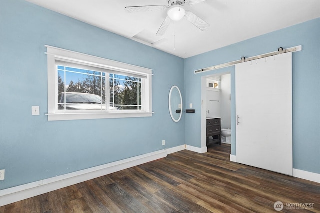 unfurnished bedroom featuring a barn door, ceiling fan, connected bathroom, and dark hardwood / wood-style floors