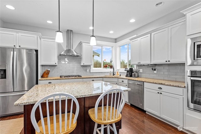 kitchen with pendant lighting, a center island, backsplash, wall chimney exhaust hood, and appliances with stainless steel finishes