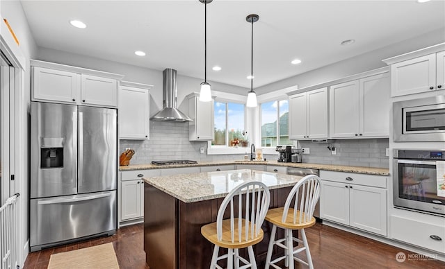 kitchen with appliances with stainless steel finishes, wall chimney exhaust hood, sink, white cabinetry, and hanging light fixtures