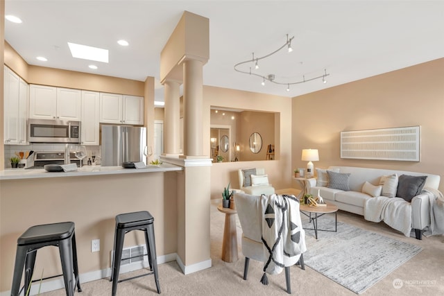 kitchen with white cabinets, ornate columns, appliances with stainless steel finishes, kitchen peninsula, and a breakfast bar area