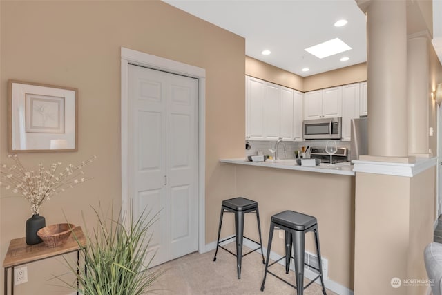 kitchen with a breakfast bar, white cabinets, a skylight, light colored carpet, and stainless steel appliances