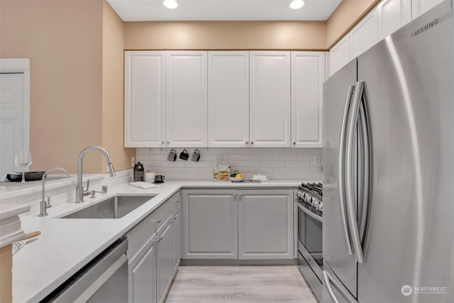 kitchen with light stone countertops, backsplash, stainless steel appliances, sink, and white cabinetry