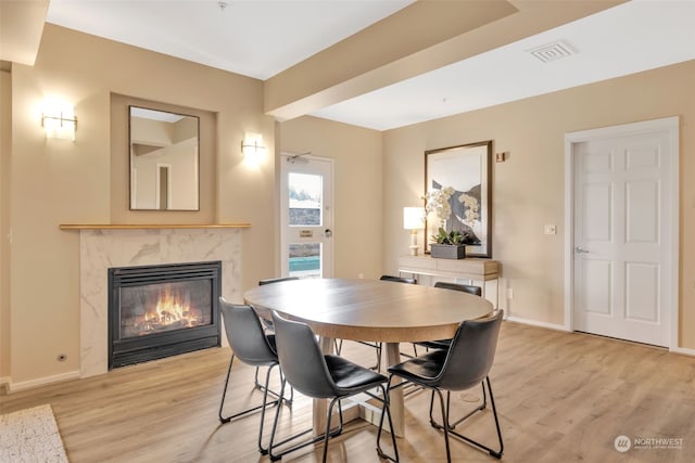 dining room featuring light wood-type flooring, ceiling fan, and a premium fireplace