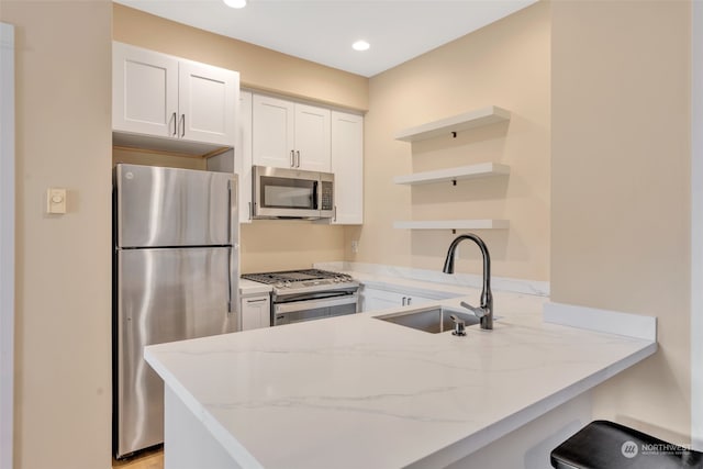 kitchen with white cabinetry, kitchen peninsula, light stone countertops, and stainless steel appliances