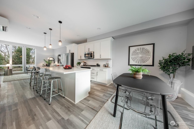 kitchen featuring white cabinetry, hanging light fixtures, stainless steel appliances, a breakfast bar area, and a kitchen island with sink