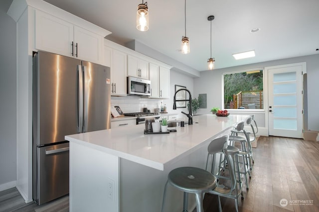 kitchen featuring stainless steel appliances, sink, pendant lighting, white cabinets, and an island with sink