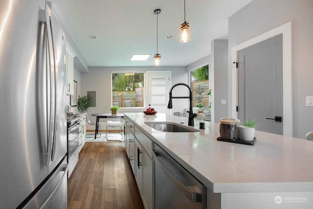 kitchen with appliances with stainless steel finishes, sink, pendant lighting, white cabinets, and an island with sink