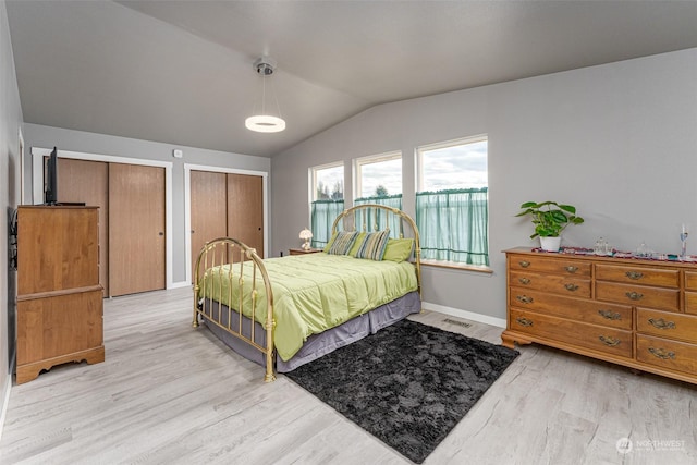 bedroom with two closets, light hardwood / wood-style flooring, and lofted ceiling