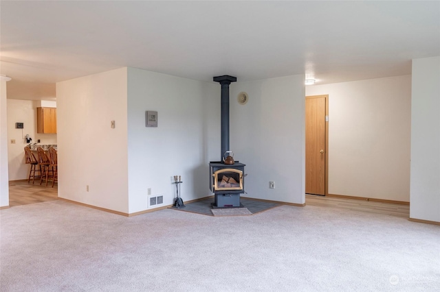 unfurnished living room with light carpet and a wood stove