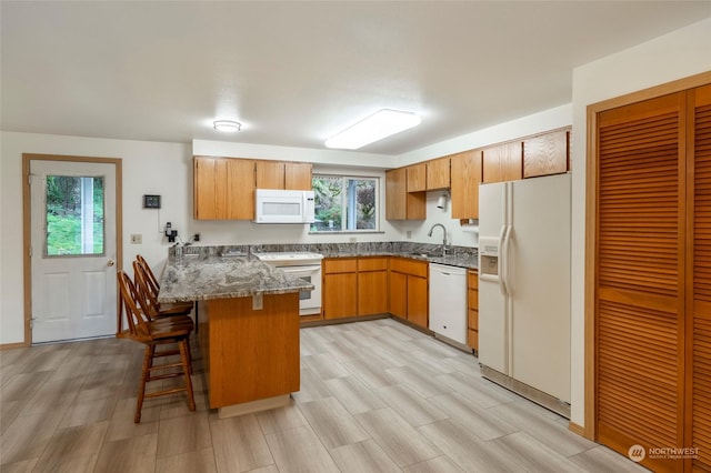 kitchen featuring kitchen peninsula, a kitchen bar, dark stone counters, white appliances, and sink