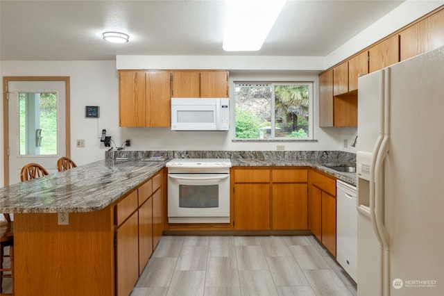 kitchen with kitchen peninsula, white appliances, stone counters, and a breakfast bar