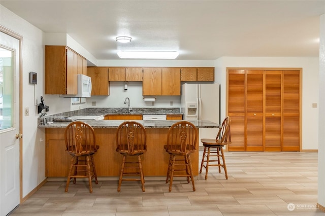 kitchen featuring sink, kitchen peninsula, stone countertops, white appliances, and a kitchen bar