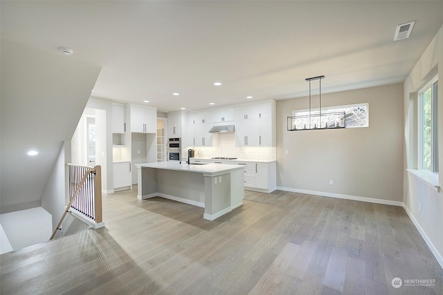 kitchen with cooktop, light wood-style flooring, white cabinets, and a sink