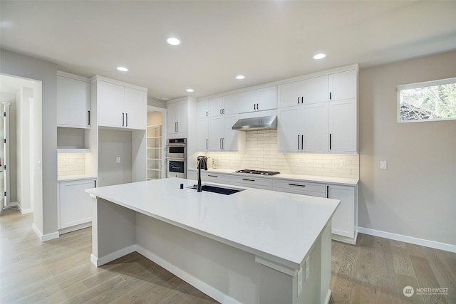 kitchen featuring a kitchen island with sink, a sink, stainless steel appliances, extractor fan, and light wood-style floors