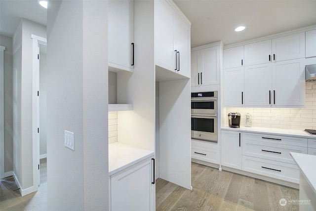 kitchen with light wood-type flooring, backsplash, double oven, white cabinets, and light countertops