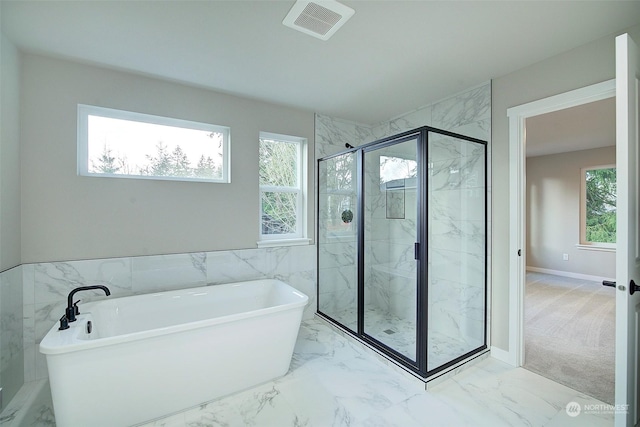 bathroom with visible vents, plenty of natural light, a soaking tub, and marble finish floor