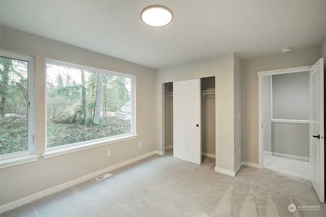 unfurnished bedroom featuring light colored carpet, visible vents, a closet, and baseboards