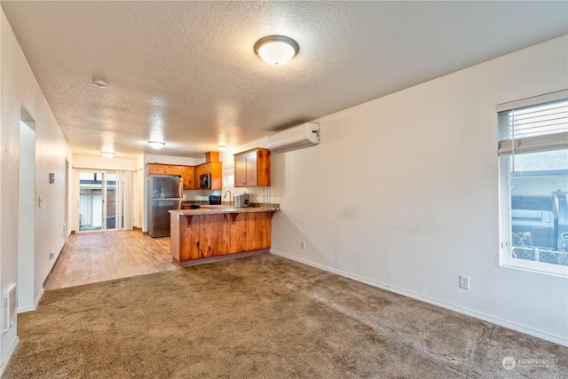 kitchen featuring a wall mounted air conditioner, a textured ceiling, appliances with stainless steel finishes, light colored carpet, and kitchen peninsula