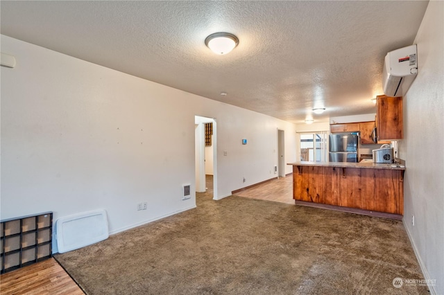 kitchen featuring kitchen peninsula, a textured ceiling, stainless steel refrigerator, and an AC wall unit