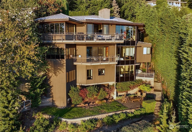 back of house featuring a chimney, metal roof, a balcony, and a standing seam roof