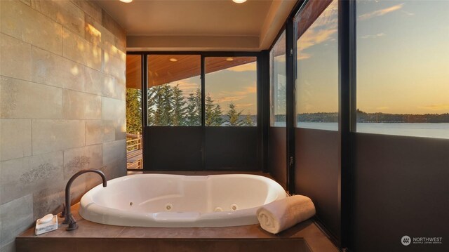 bathroom with a water view, tile walls, and a whirlpool tub