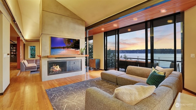 living room with a warm lit fireplace, vaulted ceiling, and wood finished floors