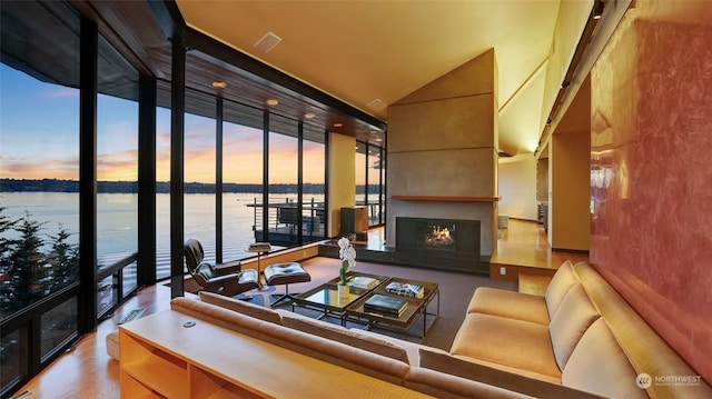 living room with a fireplace, a water view, a high ceiling, and a wall of windows