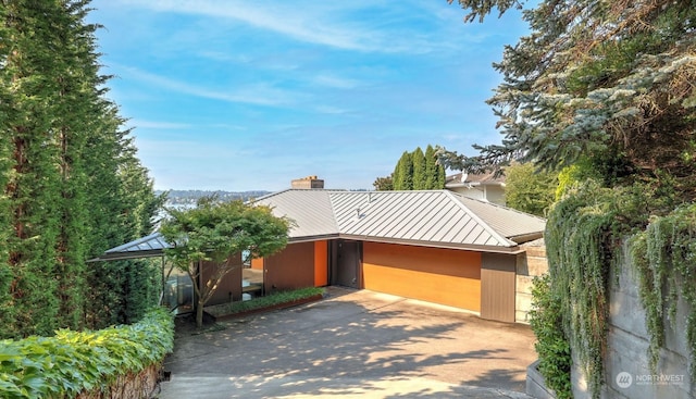 view of front of home featuring a chimney, metal roof, a standing seam roof, and concrete driveway