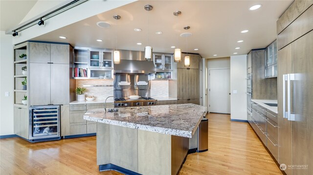 kitchen with pendant lighting, wall chimney range hood, wine cooler, light hardwood / wood-style flooring, and a large island