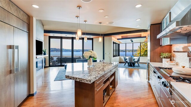 kitchen with floor to ceiling windows, stainless steel built in refrigerator, wall chimney range hood, pendant lighting, and a kitchen island