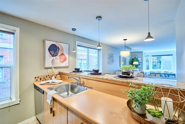 kitchen featuring dishwasher, light brown cabinetry, hanging light fixtures, and sink