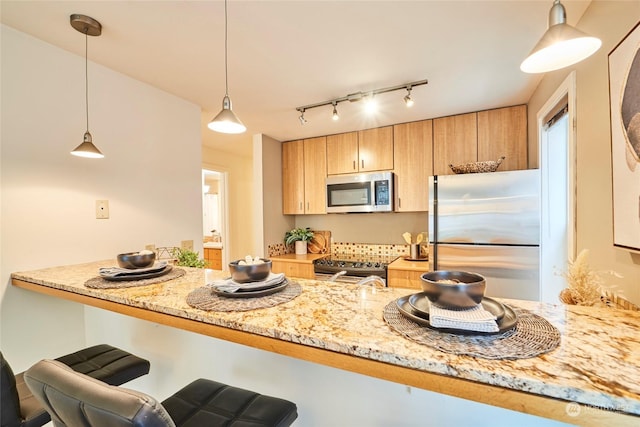 kitchen featuring kitchen peninsula, a kitchen bar, light stone counters, stainless steel appliances, and decorative light fixtures