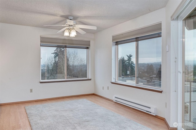 unfurnished room with a ceiling fan, a baseboard heating unit, a textured ceiling, wood finished floors, and baseboards