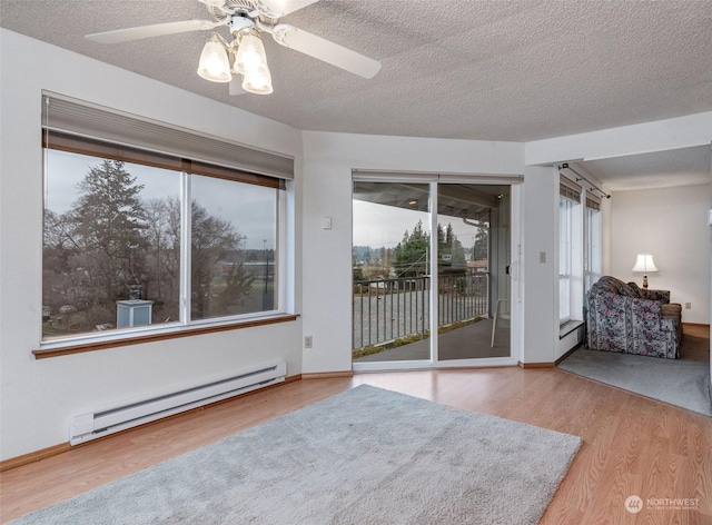 spare room with a ceiling fan, a baseboard heating unit, a textured ceiling, wood finished floors, and baseboards