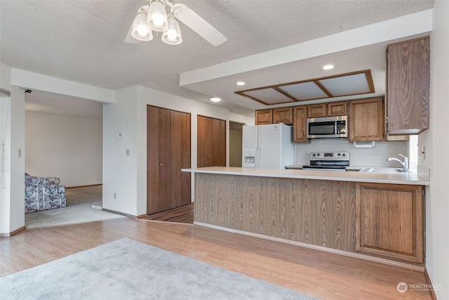 kitchen featuring light wood-style flooring, stainless steel appliances, brown cabinets, and a sink