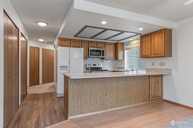 kitchen featuring stainless steel appliances, brown cabinets, light wood-style flooring, and light countertops