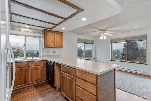 kitchen featuring a peninsula, a sink, dishwasher, brown cabinets, and baseboard heating