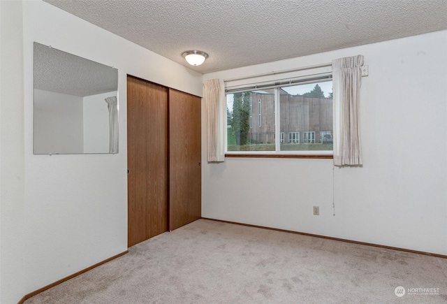 unfurnished bedroom with a closet, a textured ceiling, light carpet, and baseboards