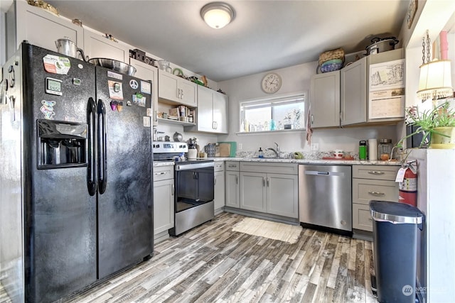 kitchen with light stone counters, light wood-type flooring, gray cabinetry, appliances with stainless steel finishes, and sink