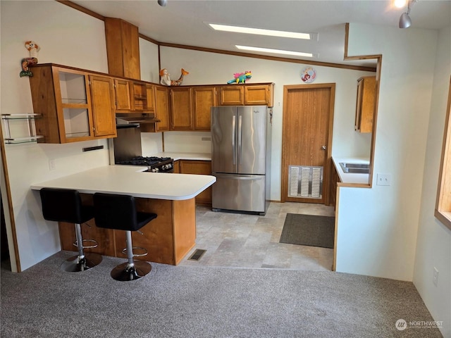 kitchen featuring stove, vaulted ceiling, kitchen peninsula, a breakfast bar area, and stainless steel refrigerator