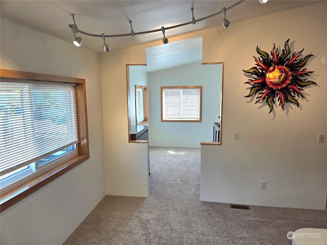 corridor with carpet floors, rail lighting, and lofted ceiling