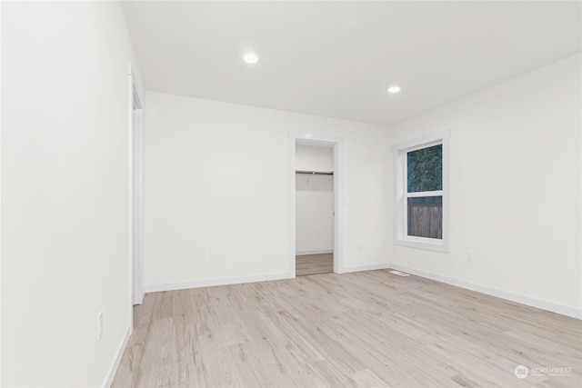 unfurnished bedroom with light hardwood / wood-style floors, a spacious closet, and a closet