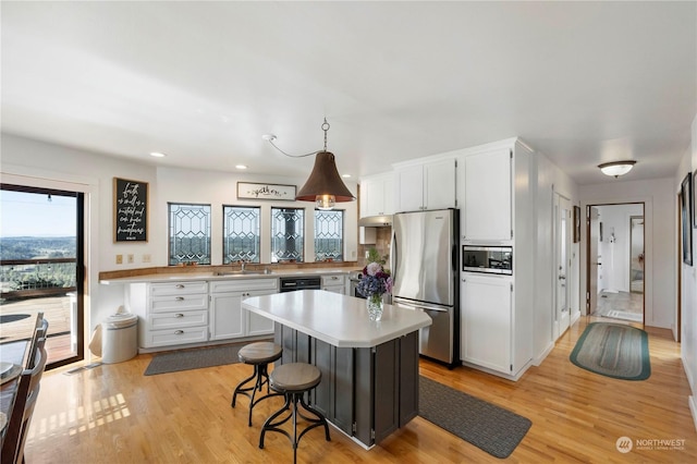 kitchen with stainless steel fridge, built in microwave, decorative light fixtures, white cabinetry, and a breakfast bar area