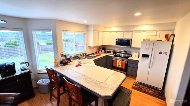 kitchen featuring a breakfast bar, stainless steel appliances, sink, light hardwood / wood-style flooring, and white cabinetry