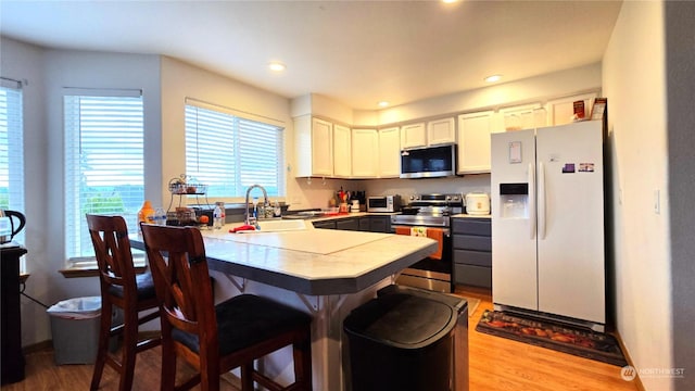 kitchen featuring sink, stainless steel appliances, light hardwood / wood-style flooring, a kitchen bar, and white cabinets