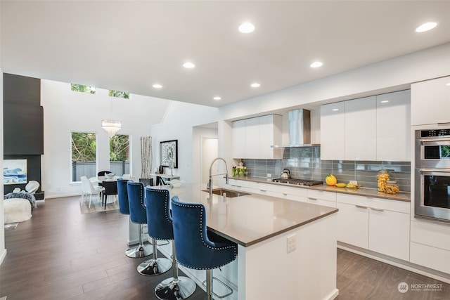 kitchen featuring white cabinets, an island with sink, wall chimney exhaust hood, and sink