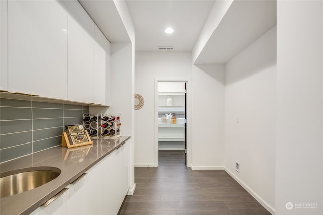 bar featuring white cabinets, decorative backsplash, sink, and dark wood-type flooring