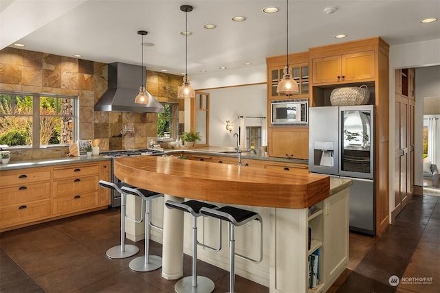 kitchen with a center island, wall chimney range hood, wood counters, a breakfast bar area, and appliances with stainless steel finishes