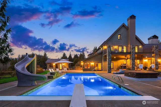 pool at dusk featuring a diving board, a water slide, a jacuzzi, an outdoor structure, and a patio