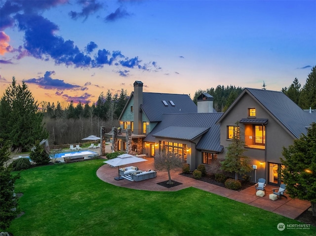 back house at dusk featuring a lawn, a swimming pool, a patio, and exterior kitchen